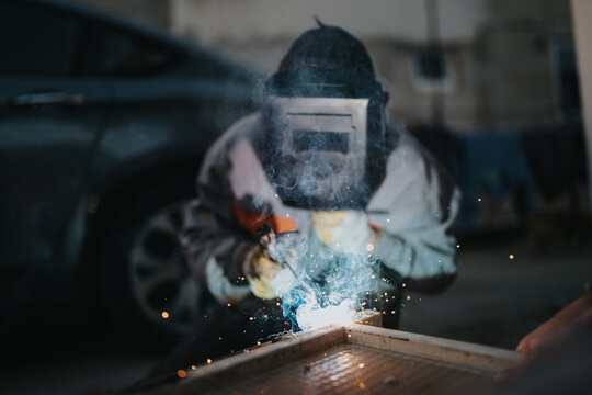 Bright sparks fly as a welder in protective gear works on a metal project. The scene emphasizes concentration, craftsmanship, and an industrial atmosphere.