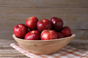 Ripe red apples in bowl on wooden table, closeup