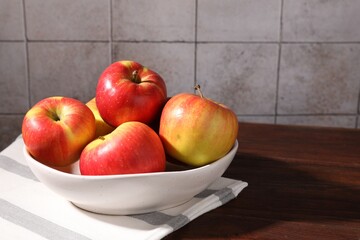 Ripe red apples in bowl on wooden table near grey tiled wall, closeup. Space for text