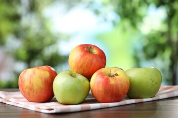 Fresh red and green apples on wooden table against blurred green background, closeup