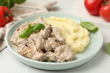 Delicious beef stroganoff with mashed potatoes and basil served on white tiled table, closeup