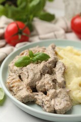 Delicious beef stroganoff with mashed potatoes and basil served on white table, closeup
