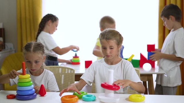 Children stack colorful ring toy while other child sorts block and toy in classroom preschool playroom setting showing play and learning activity for child development and school skill building