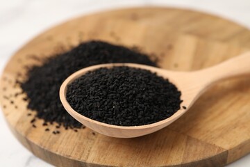 Aromatic black caraway in wooden spoon on table, closeup