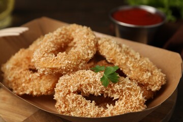 Deep fried squid rings with parsley in takeaway paper box on table, closeup