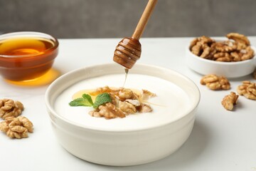 Dripping honey into Greek yogurt with walnuts and mint at white table, closeup