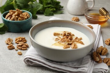 Delicious Greek yogurt with honey, nuts and mint on light grey table, closeup