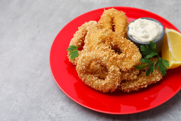 Deep fried squid rings with parsley, sauce and slice of lemon on grey textured table, closeup. Space for text