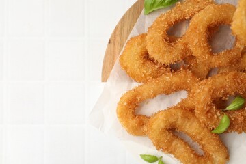 Deep fried squid rings with basil on white tiled table, top view. Space for text