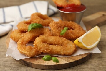 Deep fried squid rings with lemon slice, basil and ketchup on wooden table, closeup