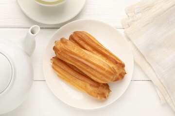Tasty eclairs served on white wooden table, flat lay