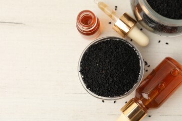 Black cumin seeds and bottles of essential oil on light wooden table, flat lay. Space for text
