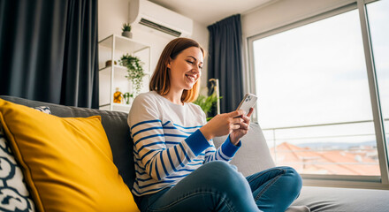 Smiling woman sitting on couch using smart phone in modern apartment home