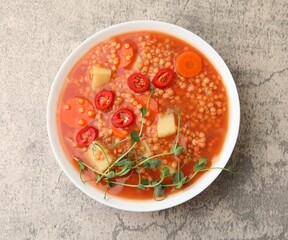 Delicious lentil soup with vegetables in bowl on grey table, top view
