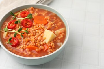 Delicious lentil soup with vegetables in bowl on white tiled table, closeup. Space for text