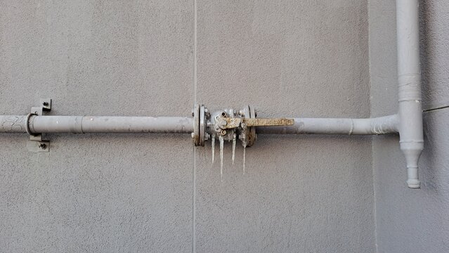 frozen water pipe with icicles on exterior building wall in winter