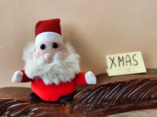 Picture of Santa Claus sitting on sofa and a placard with XMAS written on it shot during Christmas celebration
