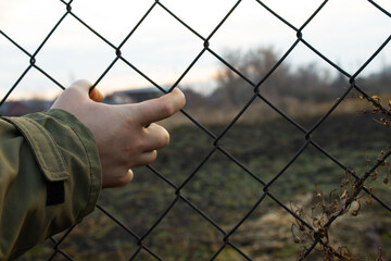 Hand Reaching Through Diamond-Patterned Chain-Link Fence