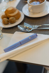 diabetes medication injection pen Ozempic soup meal restaurant table setting blue device white napkin fork close up gray placemat concept of healthcare nutrition and diet