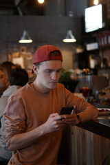 A young man holding a mobile phone while sitting in a cafe