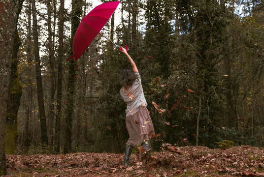 Teen girl dancing with red umbrella under falling leaves in autumn forest