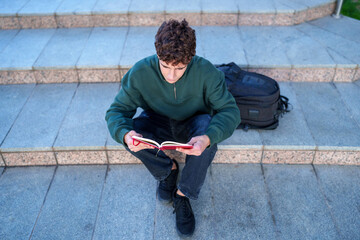 Young student reading a journal on university campus steps, focusing on studies and learning outdoors