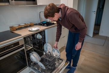 man unloading clean dishes from dishwasher in modern bright kitchen