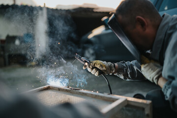 Skilled welder wearing protective gloves and a mask uses a welding torch to fuse metal, producing bright sparks in an industrial workshop. Focus on craftsmanship, safety, and industrial fabrication.
