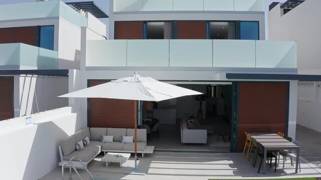 Large white patio umbrella being opened in the garden of a modern luxury villa with swimming pool and outdoor furniture, creating a relaxing and comfortable outdoor space