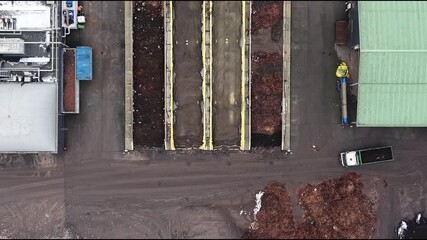 Cesis, Latvia - November 21, 2025: Aerial view of industrial site with waste piles, camera pans to reveal truck and worker, showcasing operations