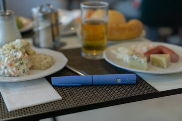 close up of a blue medication injection pen Ozempic for diabetes or weight loss placed on a napkin on a breakfast or buffet table next to two plates of food