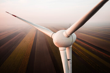 Wind turbines rising above soft morning fog, illuminated by warm golden sunrise tones. The calm landscape blends mist, light and motion, creating a serene and atmospheric view of modern renewable ener © Klima-Media