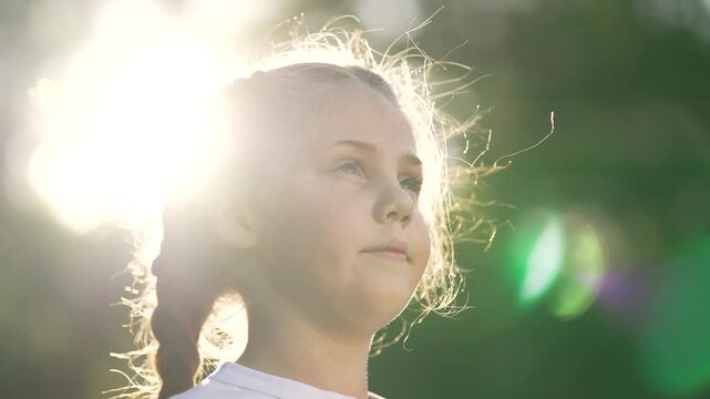 Girl closing eyes in sunlight braid hair serene child portrait with backlight and sunflare over nature backdrop soft glow on face outdoor calm expression peaceful gaze gentle breeze around face