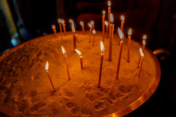 Burning prayer candles standing upright in sand © Tomasz