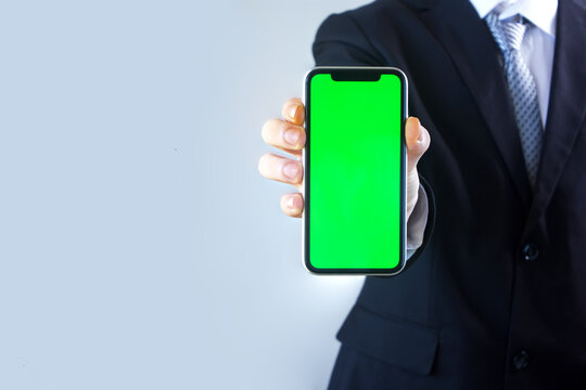 Young businessman holding green screen phone to camera.