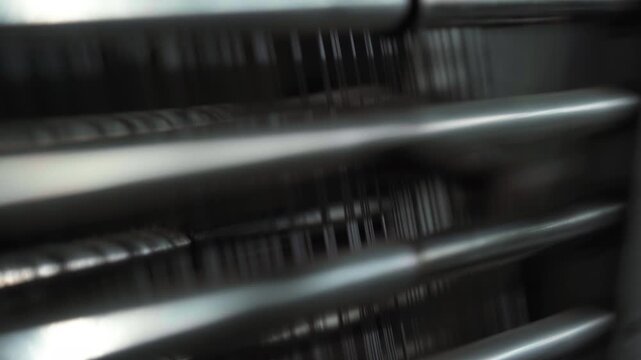 Close-up industrial loom threads in motion, cinematic macro study of stainless rods and fine filaments weaving on automated textile machine, rhythmic tension