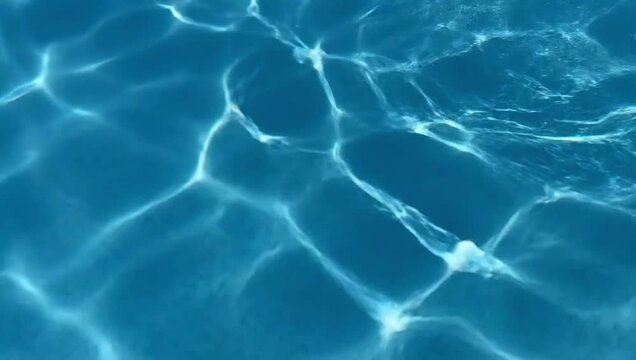 Blue swimming pool water surface with sun reflection caustics