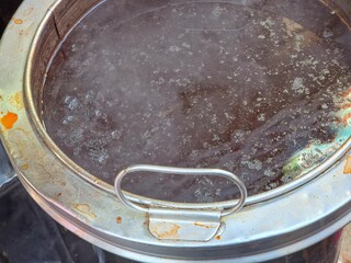 Close-up of a dark liquid, tea in a stainless steel pot or brewing vessel. 
