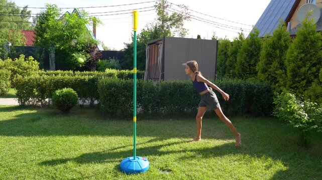 Joyful youth actively plays tetherball in vibrant, sunlit garden.