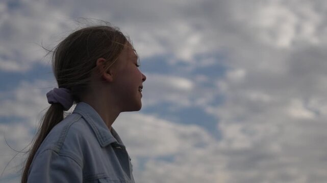 Young girl profile outdoor, happy child smiling against a beautiful cloudy sky.