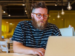 A focused designer sits at a stylish table, typing on his laptop in a contemporary coworking space filled with natural light. The ambiance is creative and inspiring, perfect for productivity
