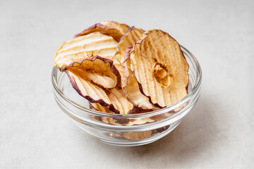 Apple chips in a glass bowl on a light gray background.