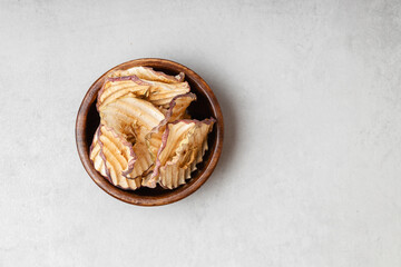 Apple dry slices in a wooden bowl on a light gray background.