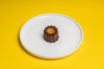 French Canelé Pastry on White Plate with Yellow Background