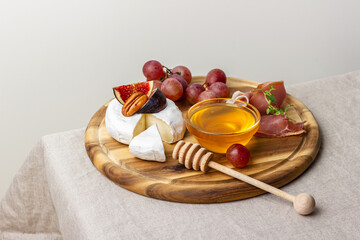 Appetizer board with meat, cheese, grapes, nuts, honey and fresh figs.