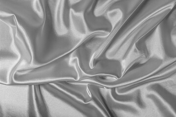 Shiny silver satin fabric is draped and wrinkled, creating a luxurious and flowing background texture.