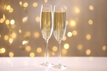 Merry Christmas and Happy New Year. Flute glasses with sparkling wine on white table against blurred lights