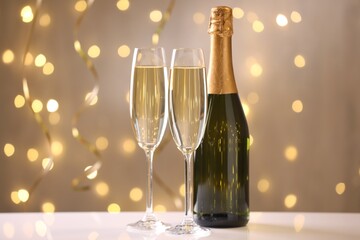 Merry Christmas and Happy New Year. Flute glasses with sparkling wine and bottle on white table against blurred lights