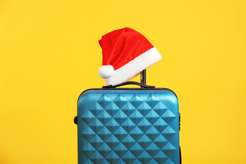 Christmas vacation. Blue suitcase with Santa hat on orange background
