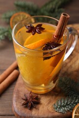 Tasty mulled wine with spices in glass cup, orange slices and fir branches on table, closeup